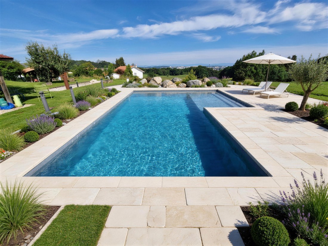 Piscine rectangulaire avec plage en pierre claire dans un jardin